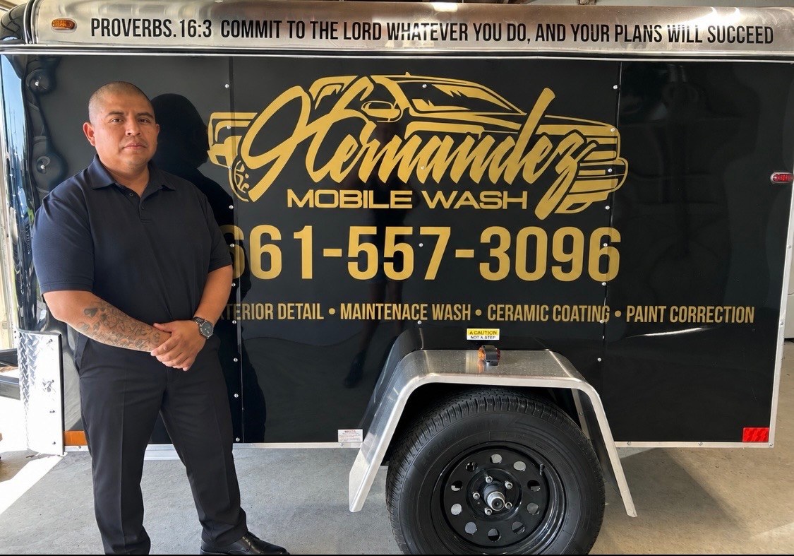 Fernando Hernandez standing in front of his black Hernandez Mobile Wash trailer with gold lettering